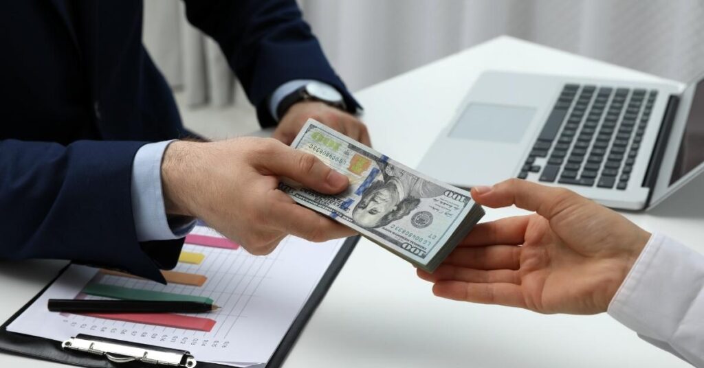 A businessman exchanging cash with another man in a professional setting, symbolizing a financial transaction.